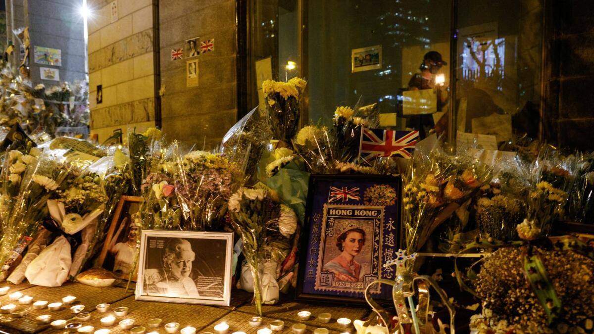 A woman holds a candle as she walks past flowers and images of Britain's Queen Elizabeth, during her funeral, outside the British Consulate-General, in Hong Kong, China