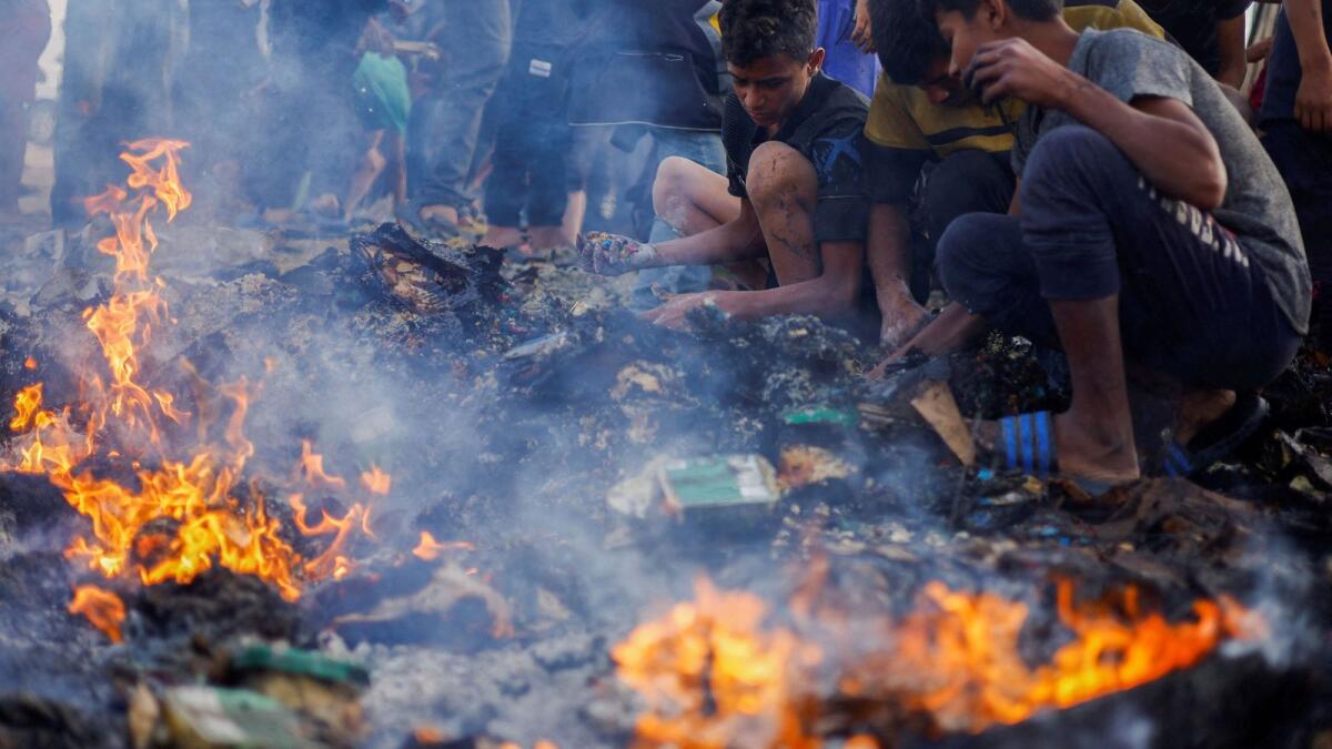 Palestinians search for food among burnt debris in the aftermath of an Israeli strike on an area designated for displaced people, in Rafah in the southern Gaza Strip, May 27, 2024. Reuters