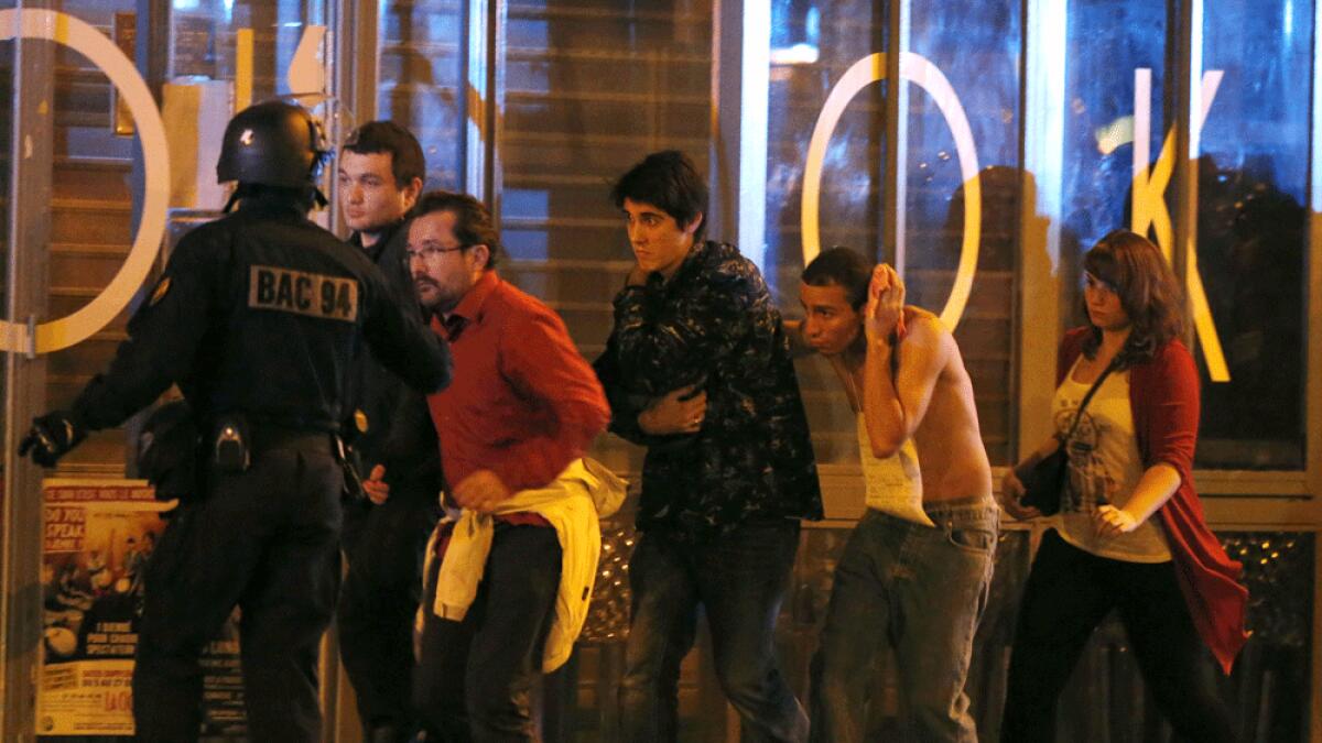 French special forces evacuate people, including an injured man holding his head, as people gather near the Bataclan concert hall following the shootings in Paris.