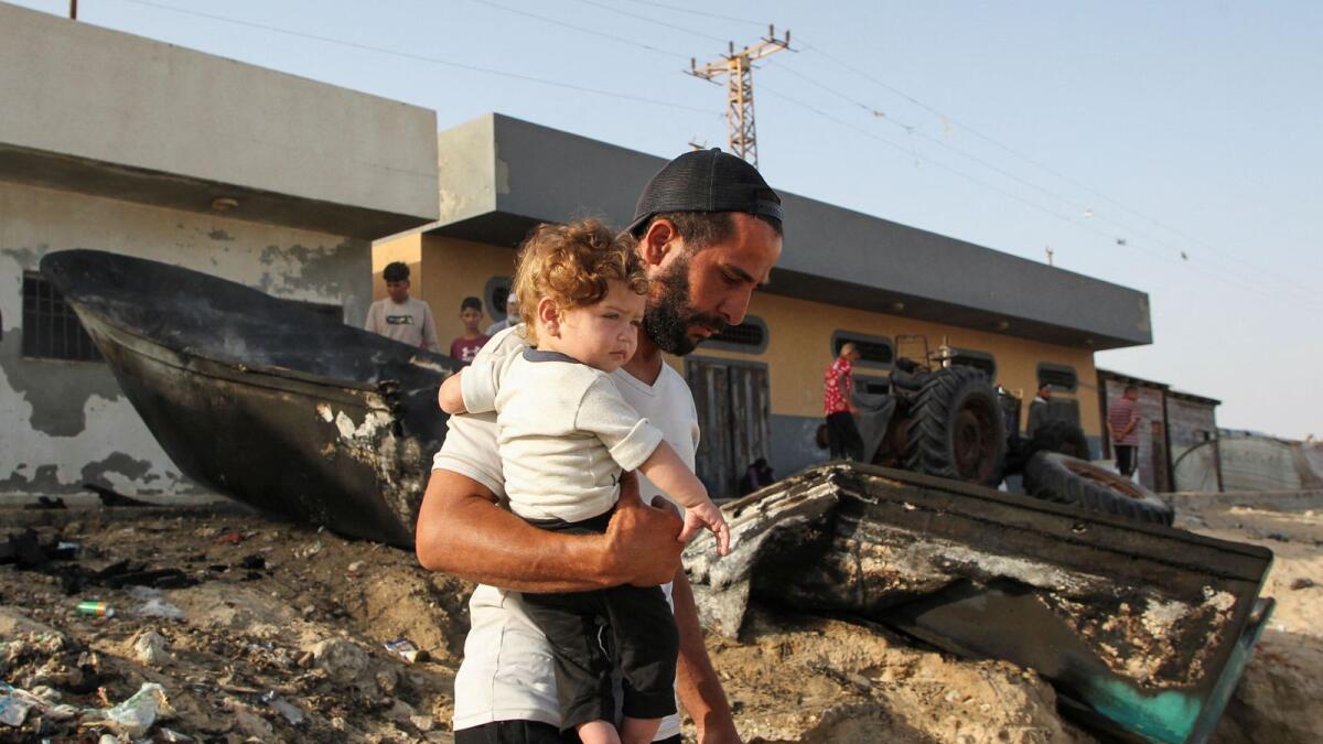 A Palestinian man holds his child as he inspects boats damaged in Israeli fire in Rafah. — Photo: Reuters
