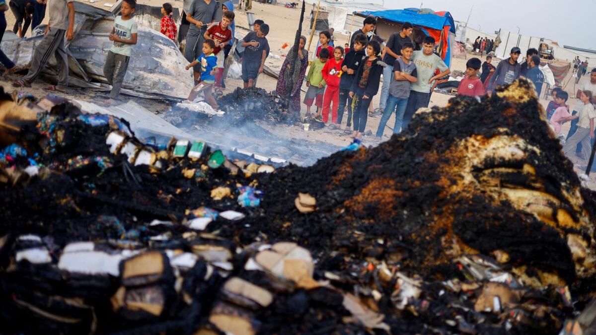 Palestinian children look at the damages while searching for food among burnt debris at the site of an Israeli strike on an area designated for displaced people, in Rafah in the southern Gaza Strip, May 27, 2024. Reuters