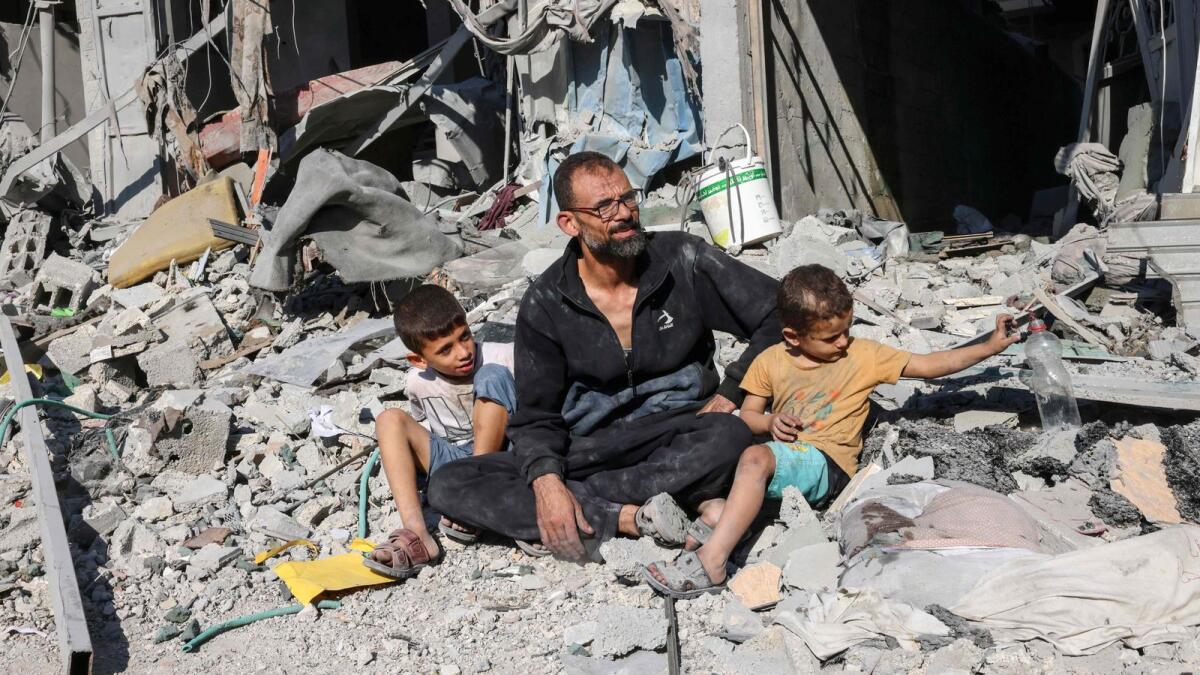 A Palestinian man sits with members of his family outside a building destroyed in an Israeli air strike in Rafah in the southern Gaza Strip on October 12. — AFP