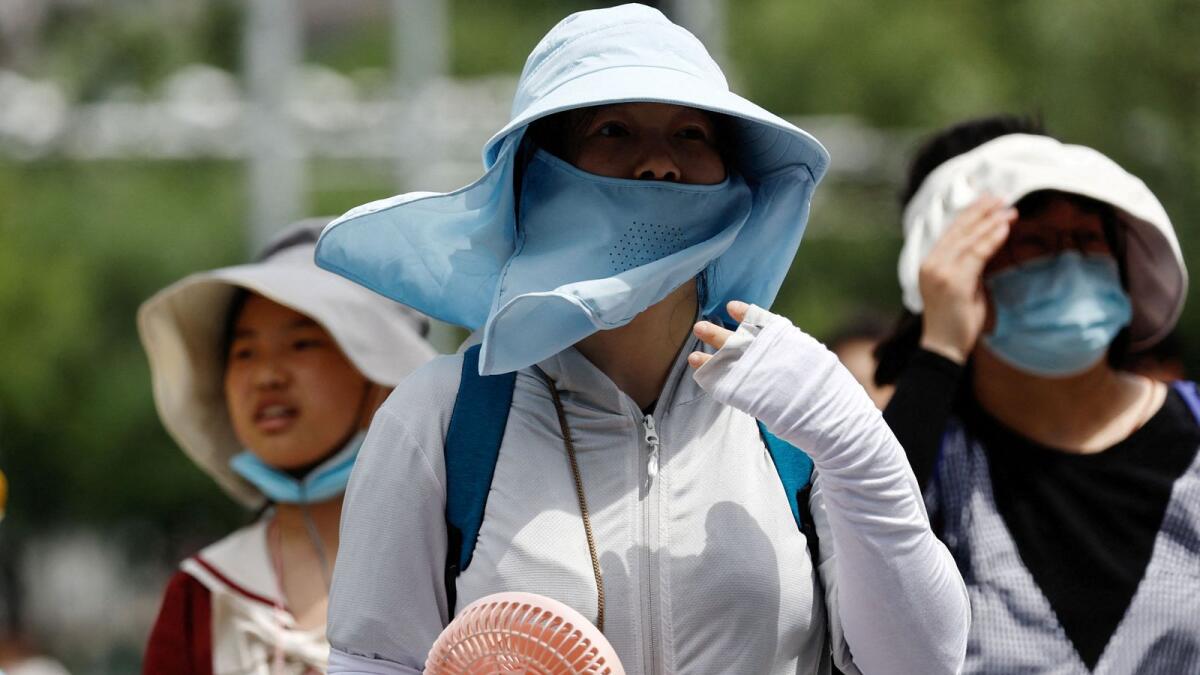FILE PHOTO: People wearing sun protection gear amid a heatwave walk on a street in Beijing, China. REUTERS File Photo