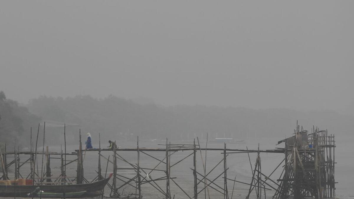 A Malaysian woman walks on a wooden jetty shrouded with haze in Port Klang, outside Kuala Lumpur, Malaysia. 