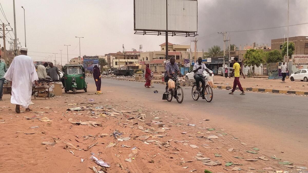 Smoke rises above buildings as people walk along a street in Omdurman. - AFP