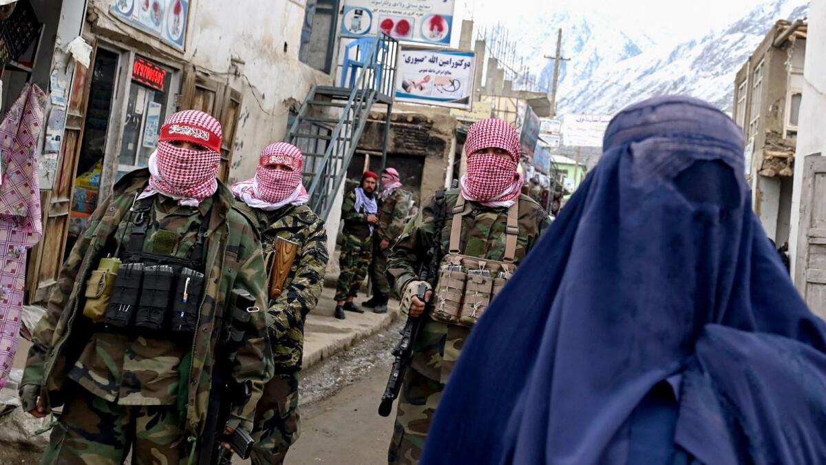 Taliban security personnel stand guard as an Afghan burqa-clad woman walks along a street at a market in the Baharak district of Badakhshan. — AFP file