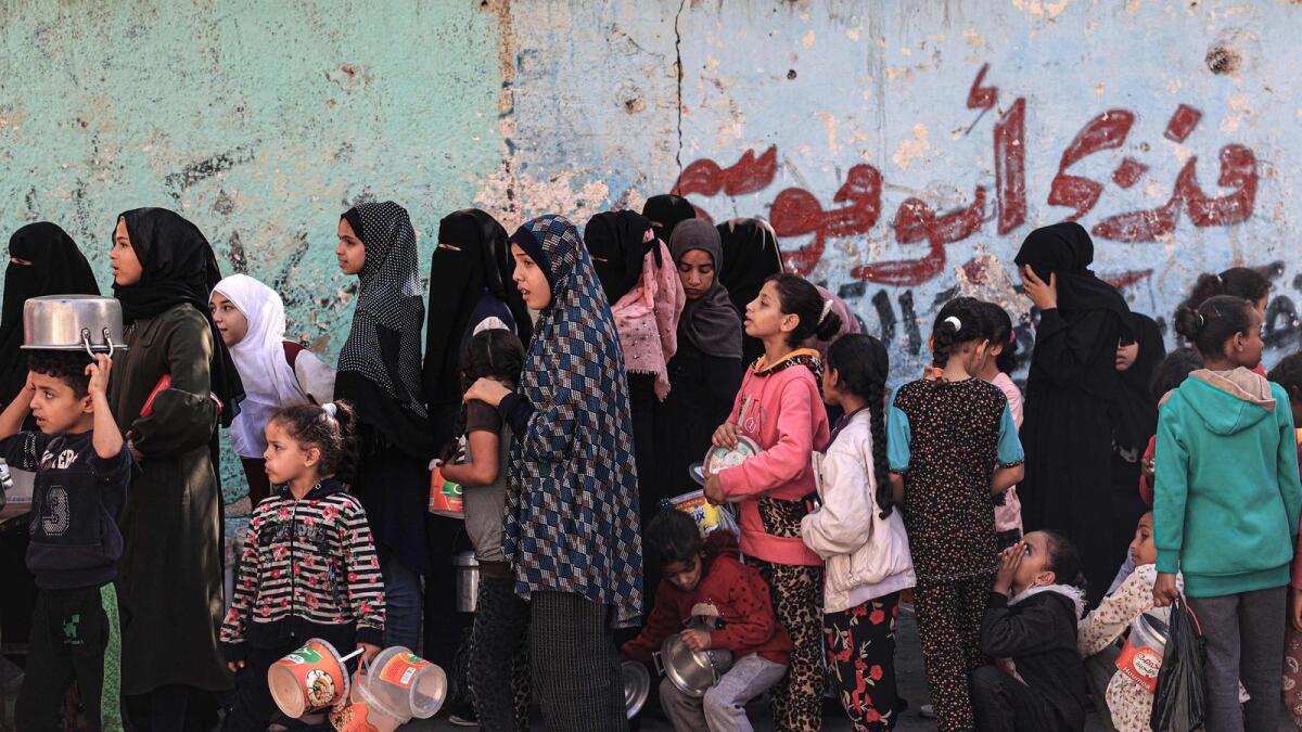 Palestinian women and children queue up to receive a portion of food at a make-shift charity kitchen in Rafah. — AFP file