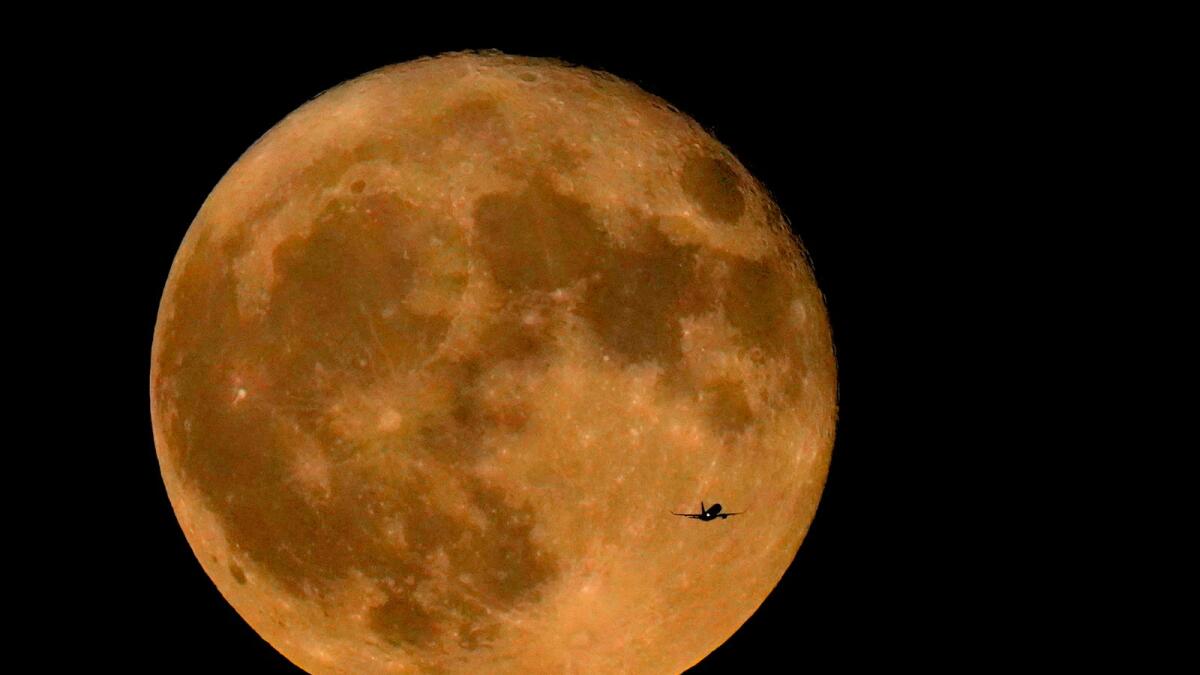A commercial airliner flies Northwest across Lake Michigan in front of the 'Full Buck' supermoon, the first of four supermoons in 2023, July 3, 2023, in Chicago. -- AP