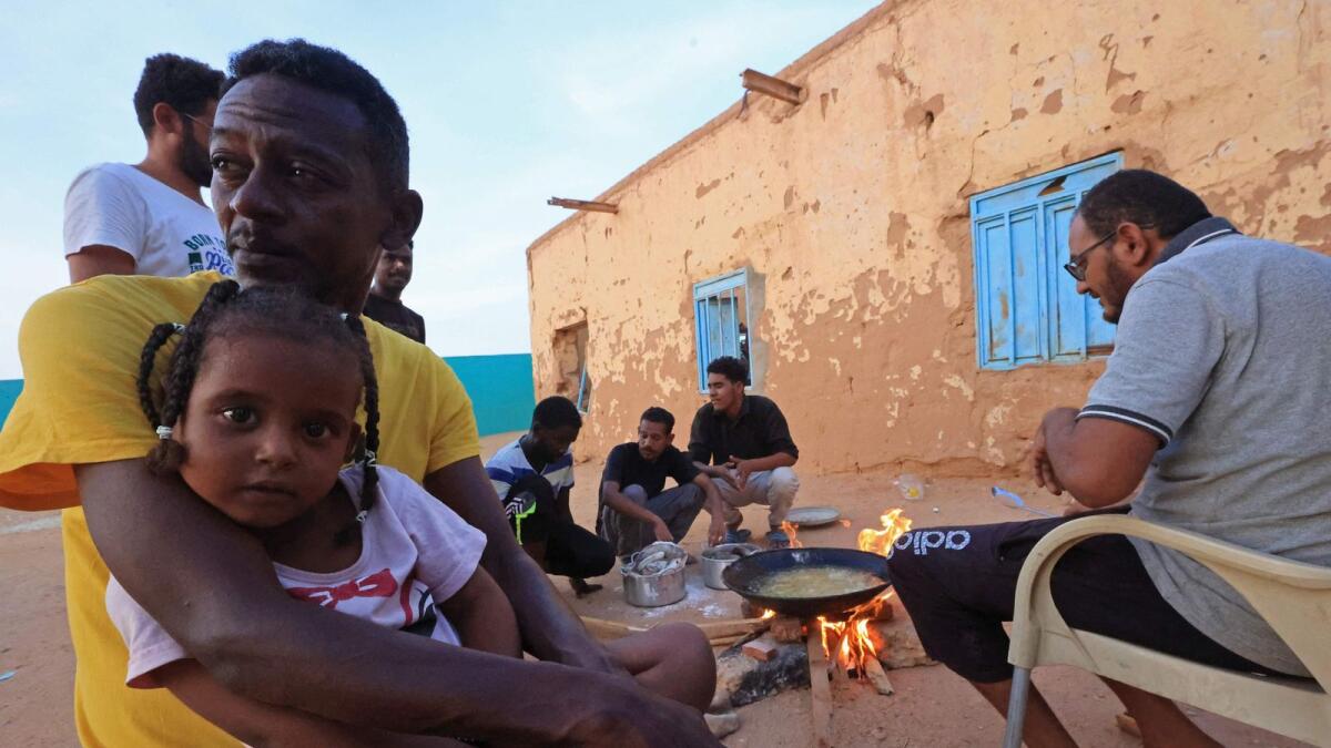 People sit around food cooking on a bonfire at a school that has been transformed into a shelter for people displaced by conflict in Sudan's northern border town of Wadi Halfa near Egypt. — AFP