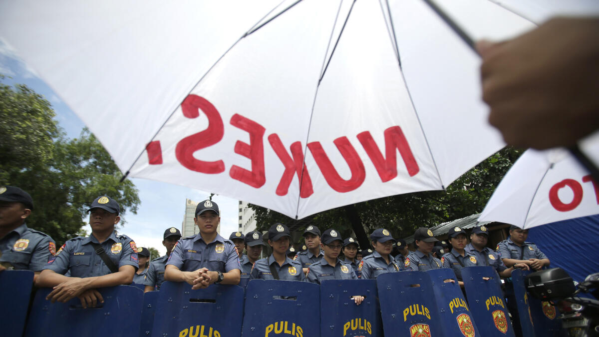 A protester holds an umbrella with slogans as Filipino police block them outside a hotel in Manila, Philippines, Tuesday, Aug. 30, 2016. AP