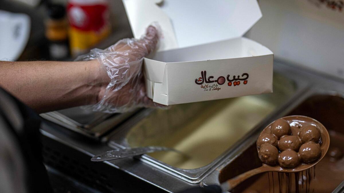 An employee submerges sweets in milk chocolate with traditional Sudanese taste at a restaurant run by a businessman who relocated to Cairo after fleeing the ongoing war in Sudan, on May 27, 2024. — AFP