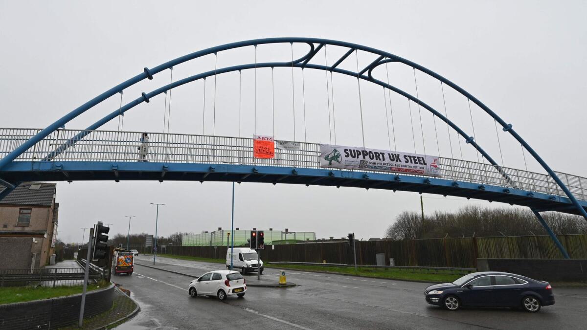 Vehicles drive under a foot bridge displaying a banner in support of the UK Steel industry near to the Tata Steel Port Talbot integrated iron and steel works in south Wales. — AFP