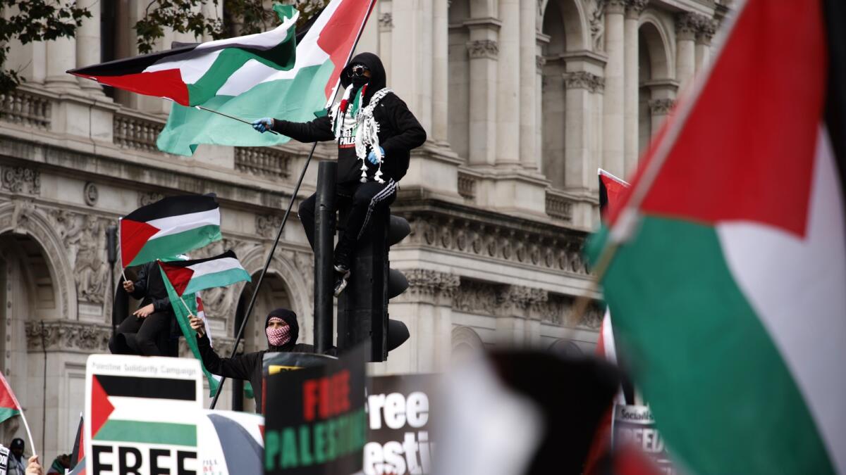Demonstrators hold up flags and placards as they stand on traffic lights near Downing Street during a pro Palestinian demonstration in London. — AP