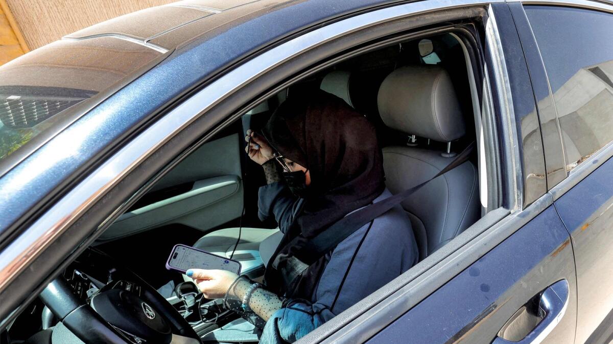 A woman browses a phone as she sits in the driver's seat of a vehicle parked along a street in Riyadh. — AFP file
