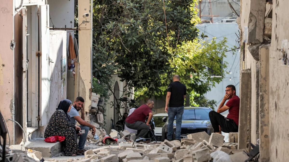 People sit by rubbles along an alleyway in the occupied West Bank city of Jenin on Wednesday after the Israeli army declared the end of a two-day military operation in the area. -- AFP