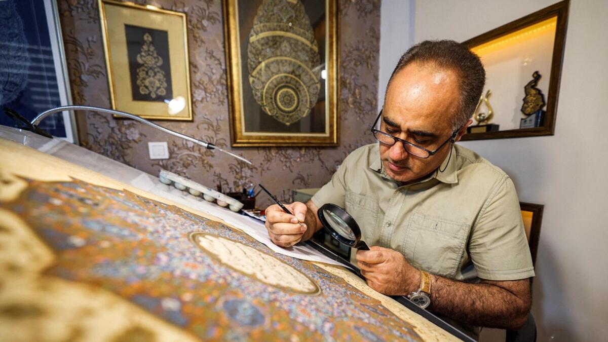 Mohammad Hossein Aghamiri uses a magnifying glass as he works on one of his pieces depicting Al Fatiha, the first chapter of the the holy Quran, at his workshop in Tehran on June 5, 2024. — AFP
