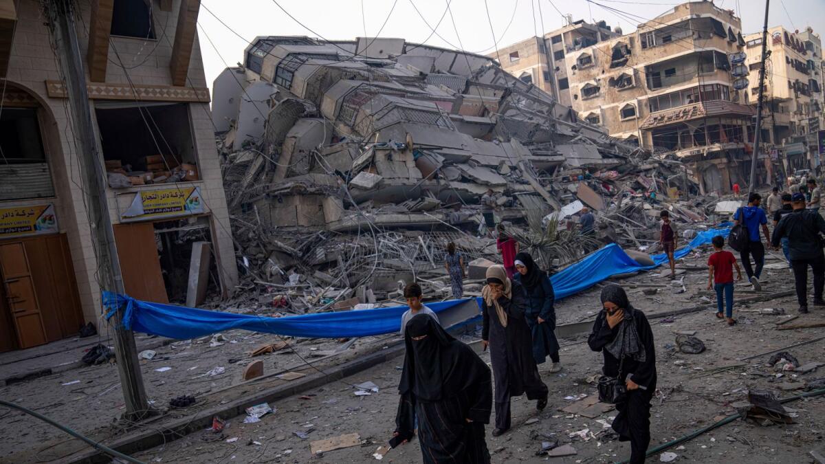 Palestinians walk by the rubble of a building after it was struck by an Israeli airstrike, in Gaza City. — AP