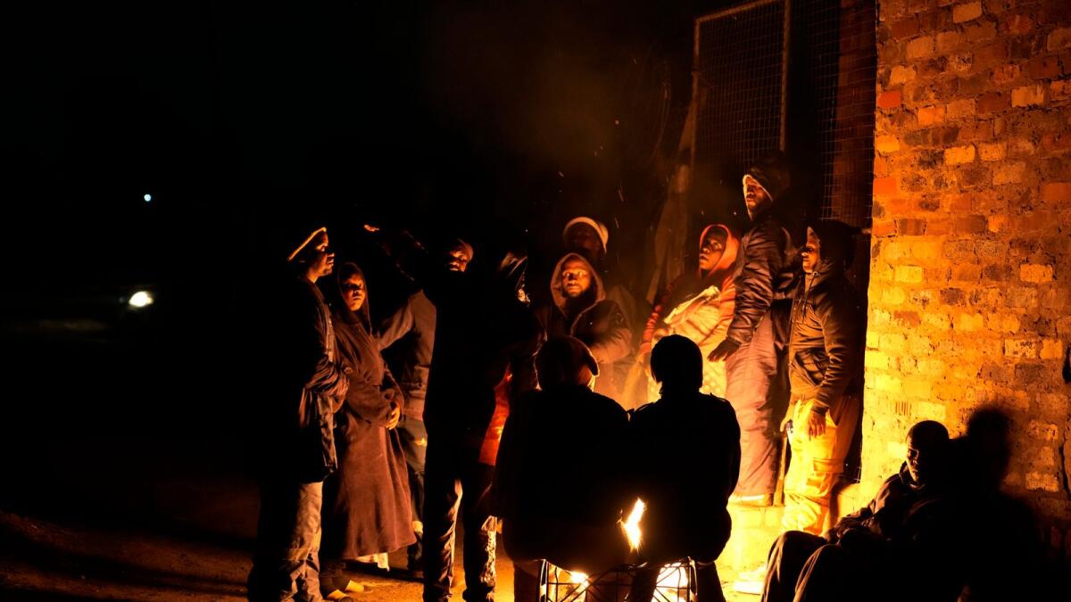 People huddle around a fire for warmth in the Angelo Informal Settlement in Boksburg, South Africa, on Thursday. Police said a gas leak left multiple people dead including children. -- AP