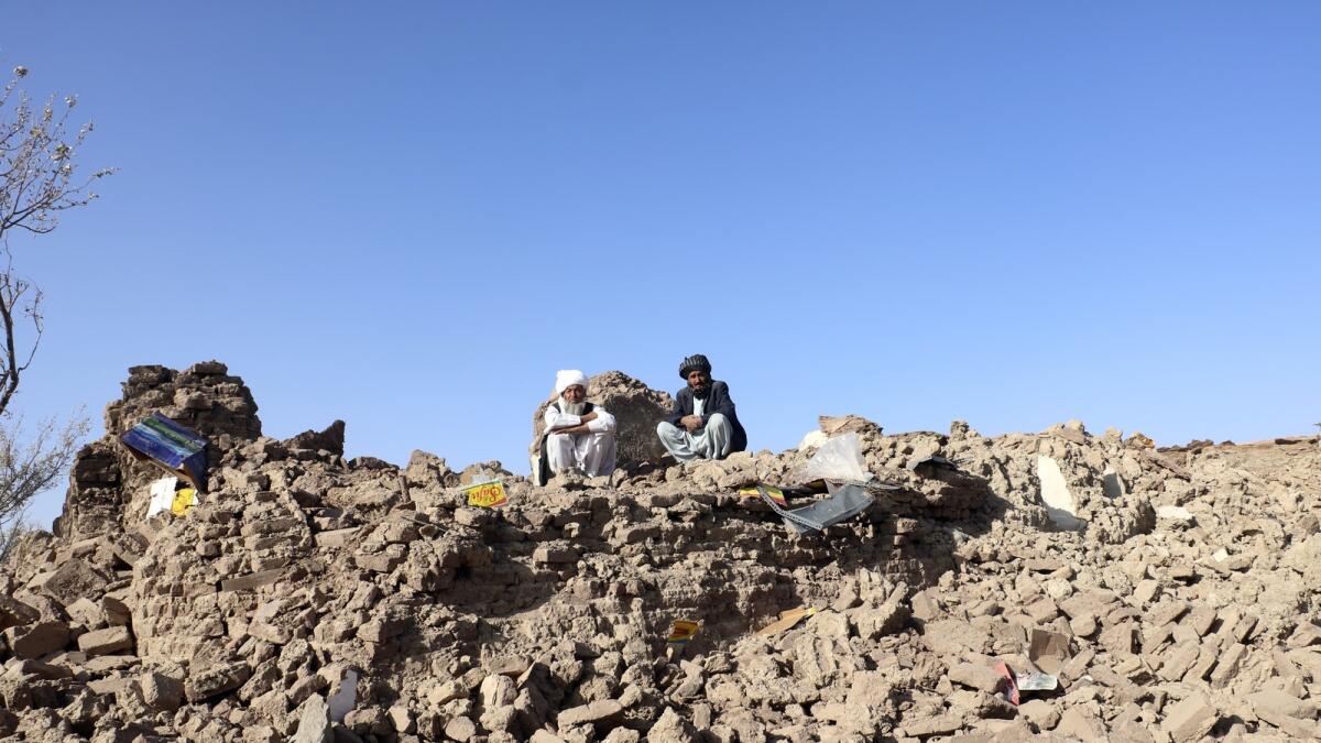 Afghan men sit on the rubble of their destroyed homes.