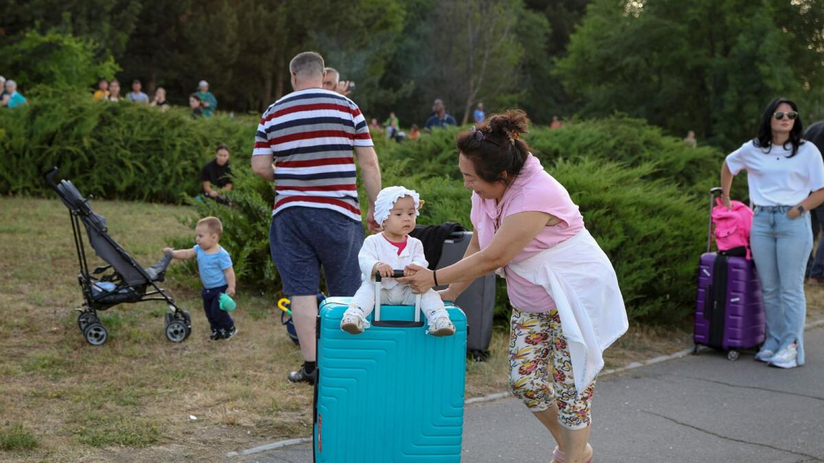 A baby sits on a suitcase as travellers stand outside the Chisinau airport in Moldova Friday, after being evacuated following a shooting inside the terminal that left two people dead. — AP