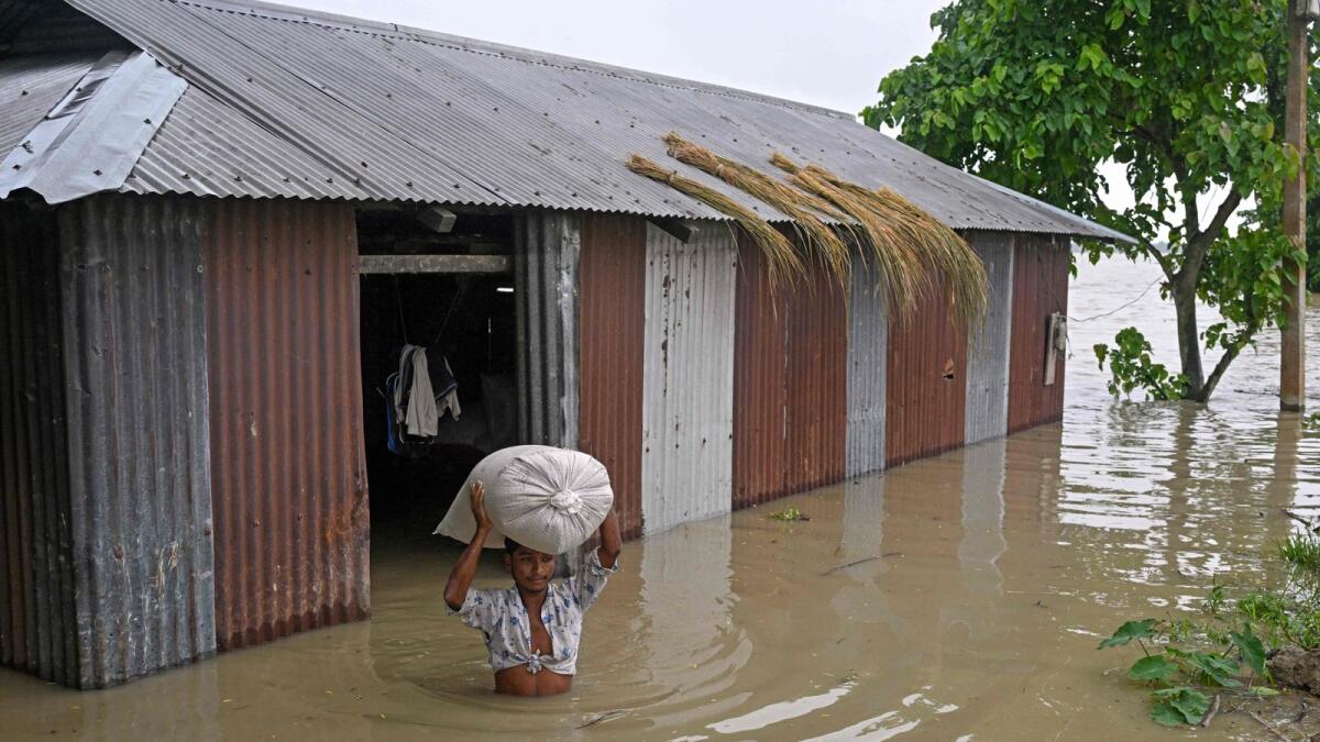 A man wades through floodwaters as he carries a sack of rice from his house deluged by heavy rain in Morigaon district in Assam, India. AFP