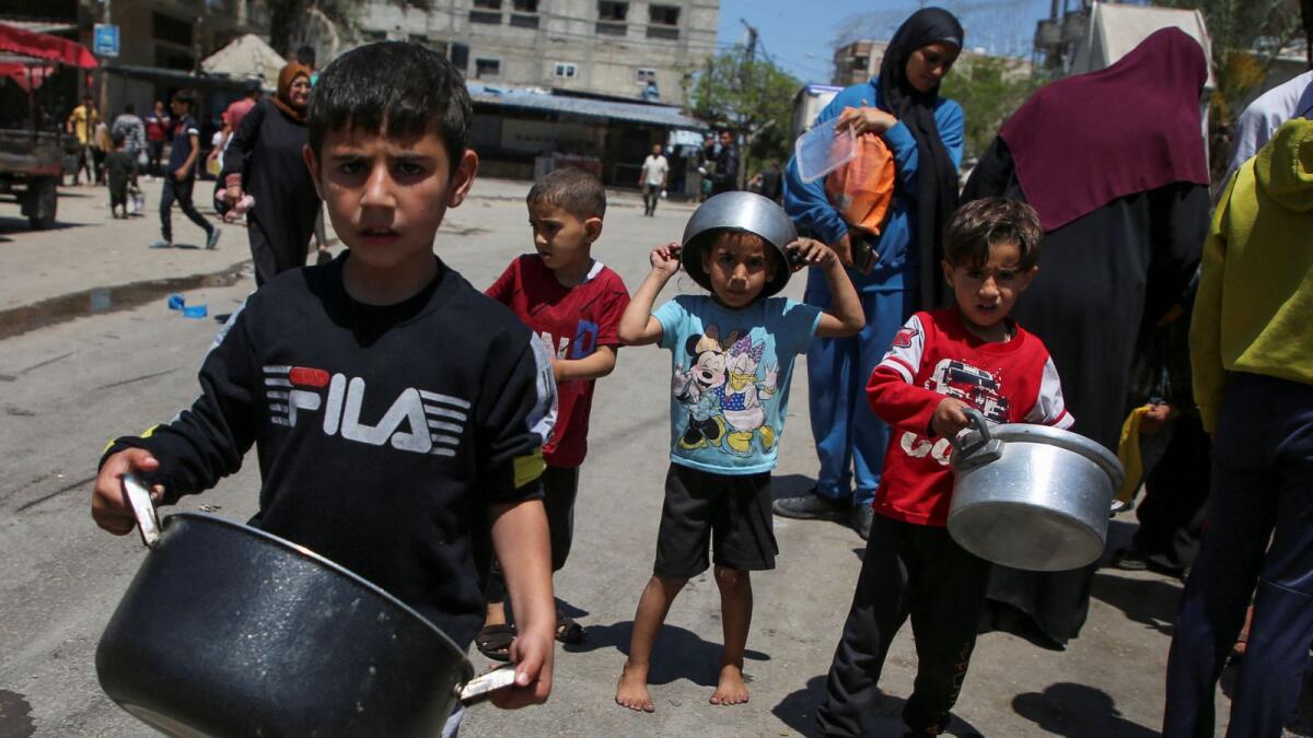 Palestinian children carrying pots wait to receive food cooked by a charity kitchen, amid shortages of aid supplies, after Israeli forces launched a ground and air operation in the eastern part of Rafah on May 8. — Photo: Reuters file