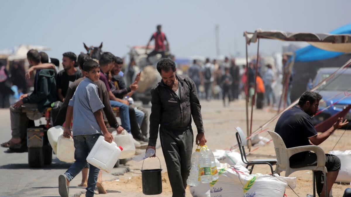 Palestinians who sought refuge in Deir Al Balah after fleeing Rafah in the southern Gaza Strip, carry water to their tents at a makeshift camp. — Photo: AFP