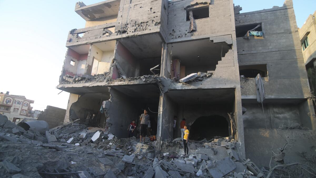 Palestinians stand by a building destroyed in an Israeli airstrike in the Rafah border, Gaza Strip, on Monday. — AP