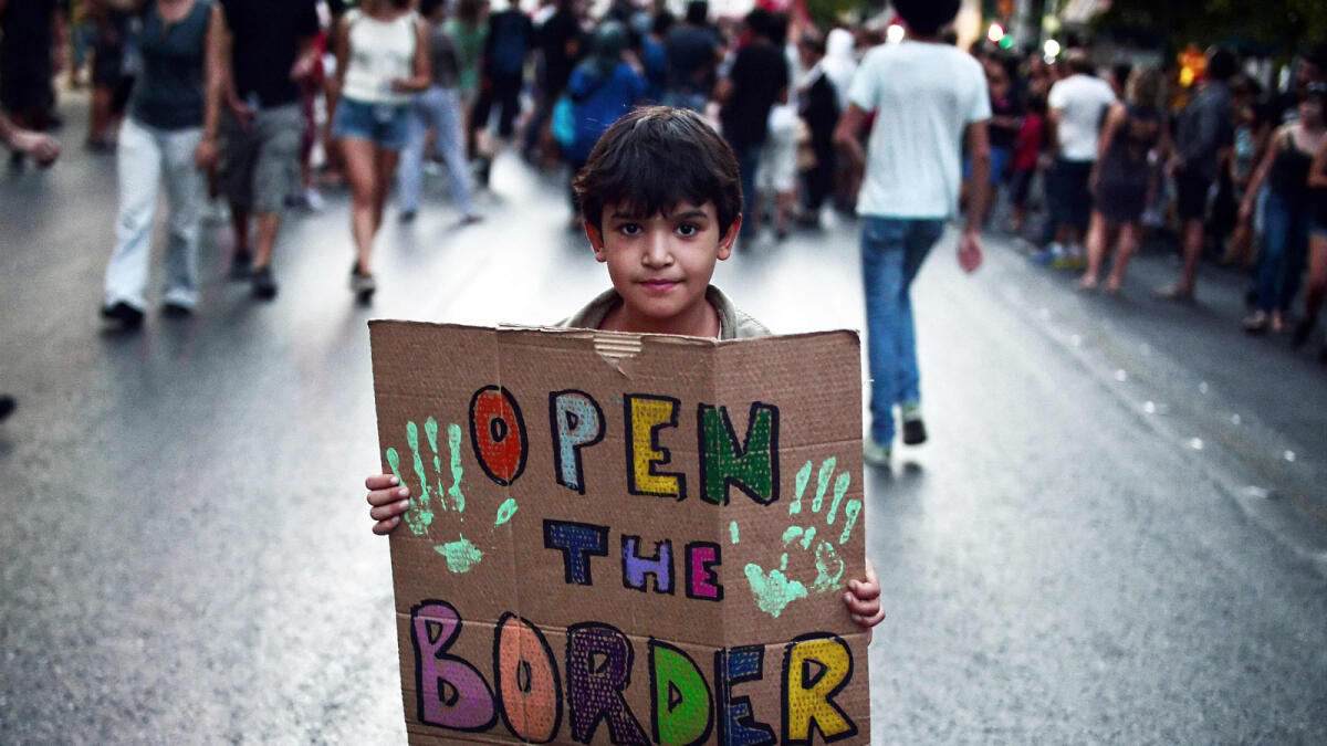 A child holds a placard reading 'Open the border' during a demonstration in support to refugees and migrants in front of Athens municipality building, in Athens, on August 29, 2016. AFP