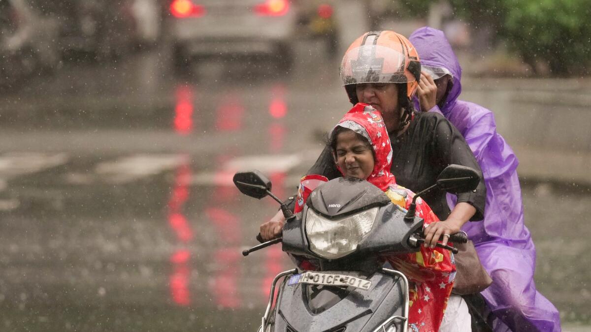 Commuters ride past during monsoon rain, in Mumbai. — PTI