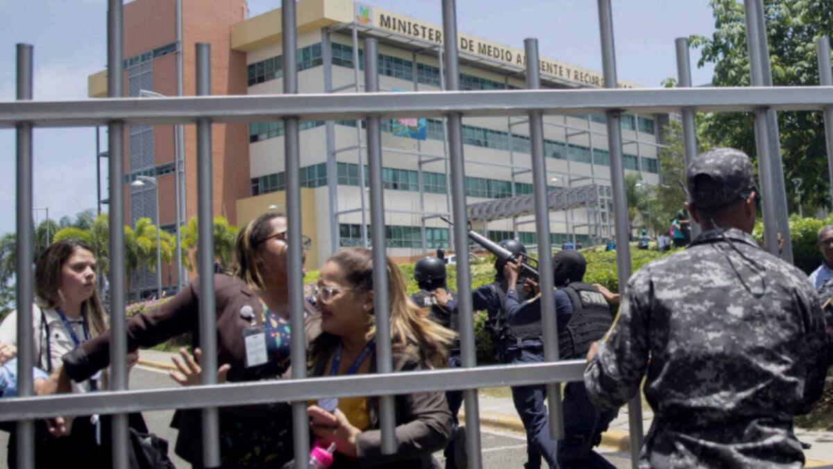 Employees of the Dominican Ministry of Environment try to get out the fence of the ministry´s building during a shooting, in Santo Domingo. — AFP