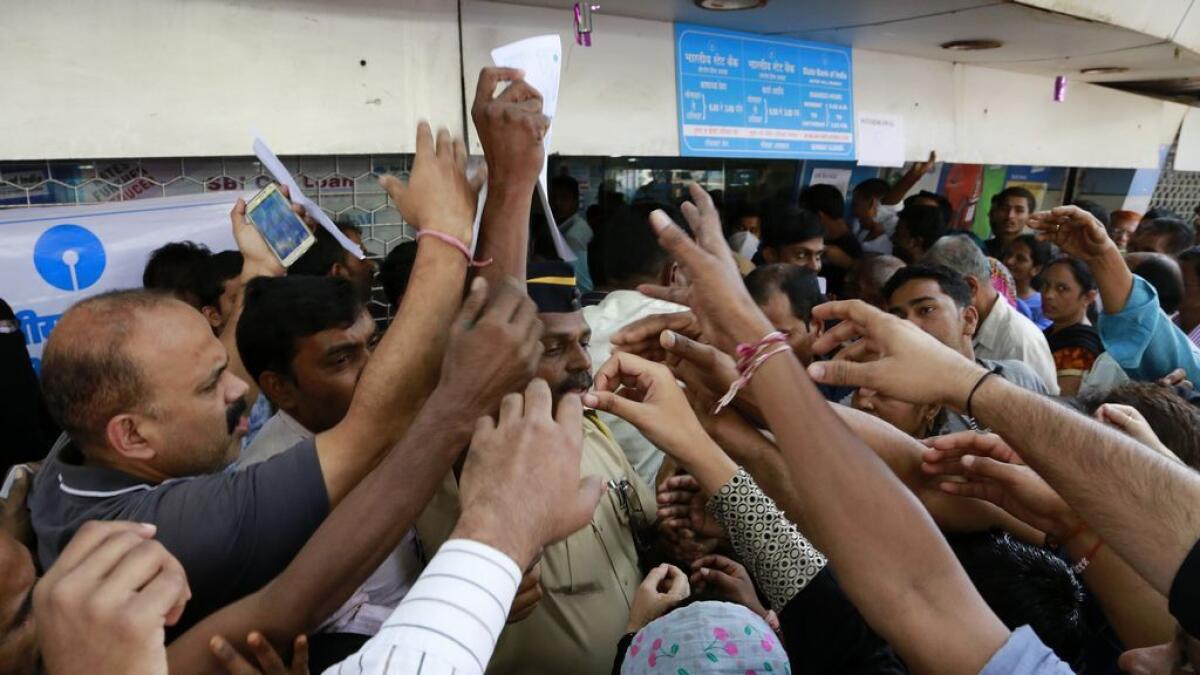 Indians stretch out their hands to collect withdrawal slips from a police officer to deposit and exchange discontinued currency notes outside the State bank of India 