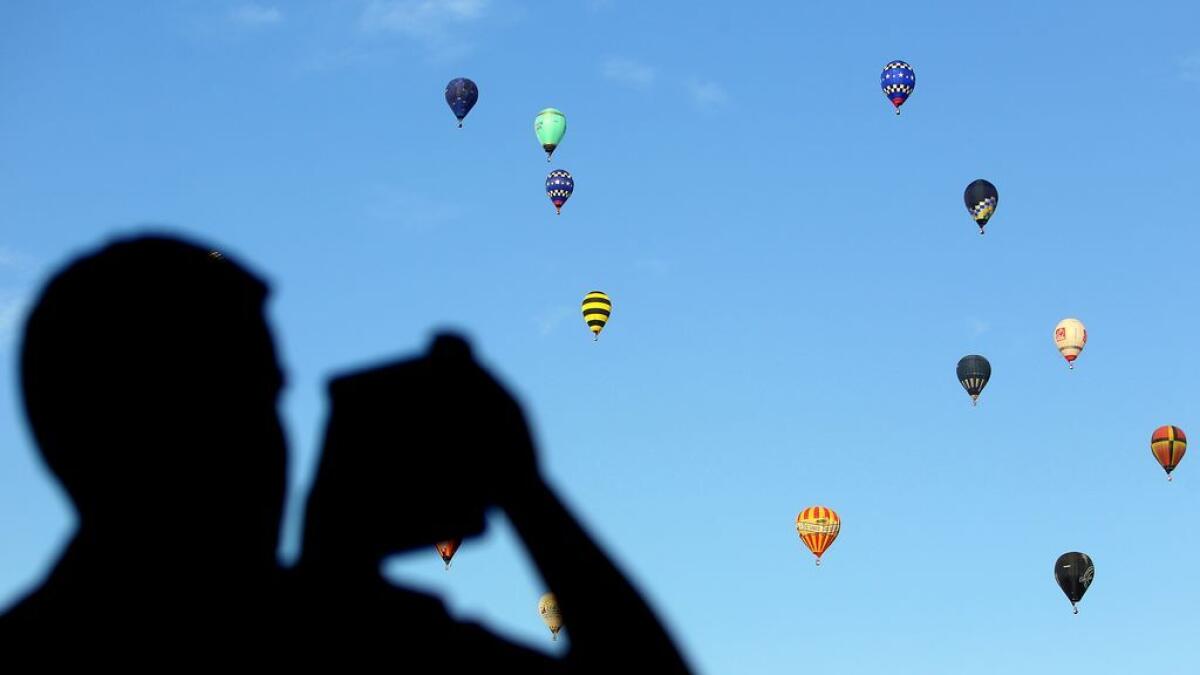 A passerby takes a picture of hot air balloons that fly over the Al Quoz area in Dubai during the World Air Games 2015, held under the rules of the Federation Aeronautique International (FAI) as part of the 'Dubai International Balloon Fiesta' event.- Photo by Kiran Prasad/Khaleej Times