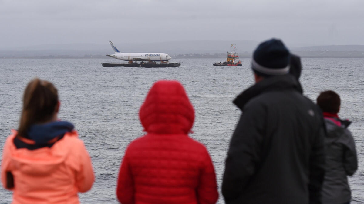 People look on as a Boeing 767 airplane arrives at Enniscrone estuary after being tugged from Shannon airport out to sea around the west coast of Ireland. - Reuters