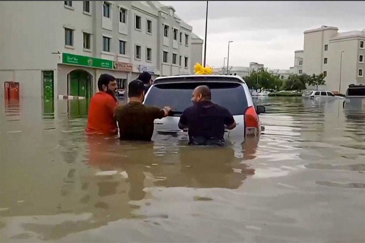 People push a stranded car along a flooded street in Dubai on April 16, 2024.Photo: AFP