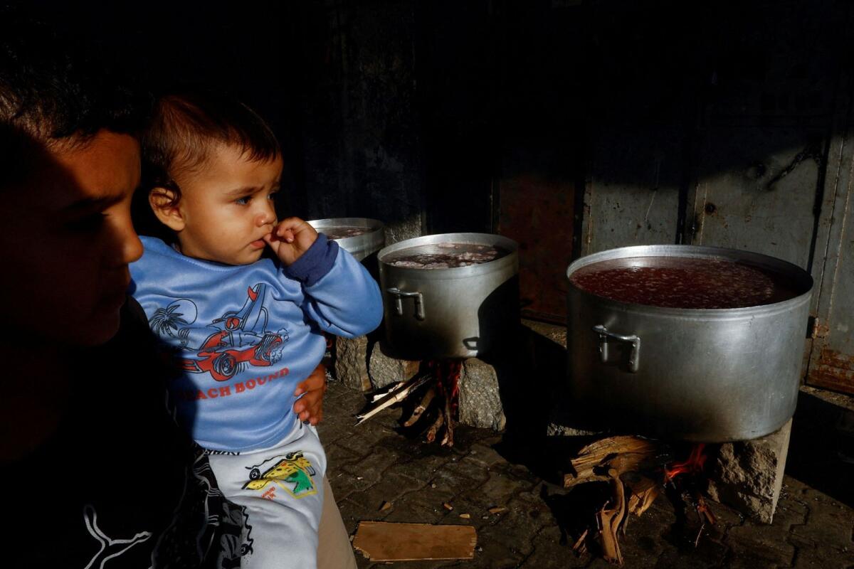 Children watch as food is cooked on firewood amid shortages of fuel and gas to provide food for Palestinians who fled their houses amid Israeli strikes in Khan Younis in the southern Gaza Strip Sunday. — Reuters