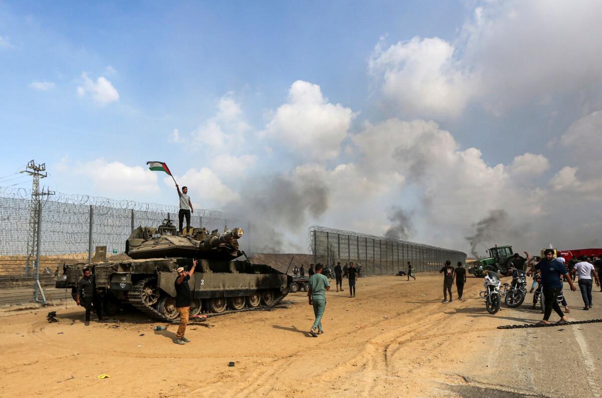 Palestinians wave their national flag and celebrate by a destroyed Israeli tank at the Gaza Strip. Photo: AP