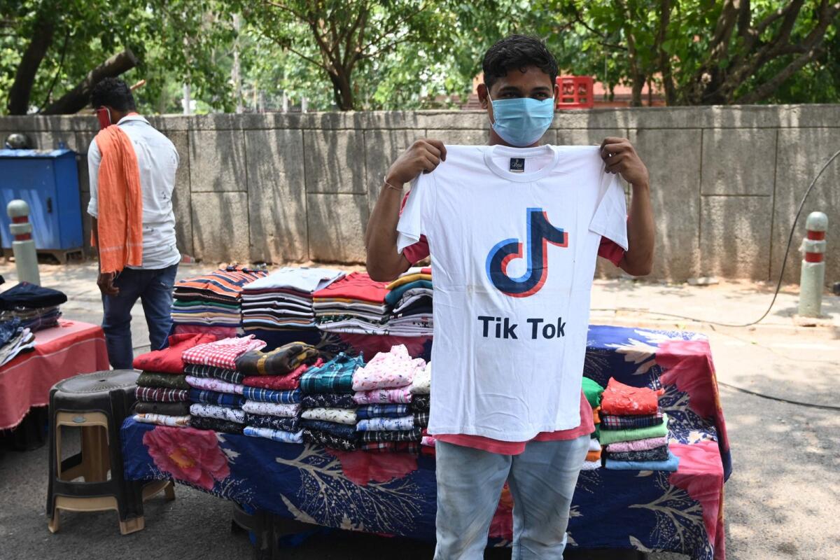 A garment street vendor poses for a picture in front of his stall with a t-shirt with the logo of the social media video-sharing application Tik Tok in New Delhi on June 30, 2020. — AFP