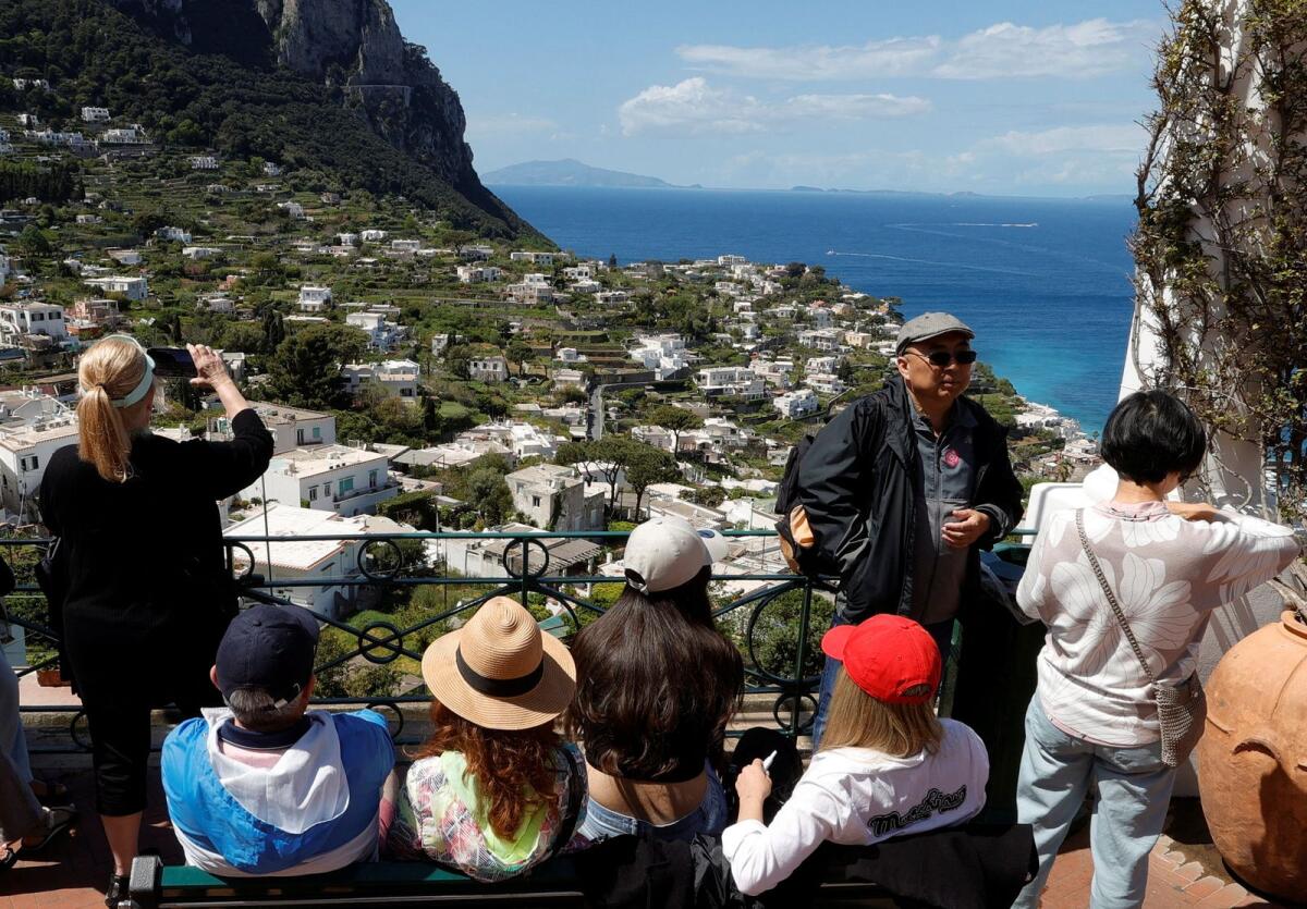 People sit on a bench and take photos on Capri Island, Italy, on April 18, 2024. — Reuters