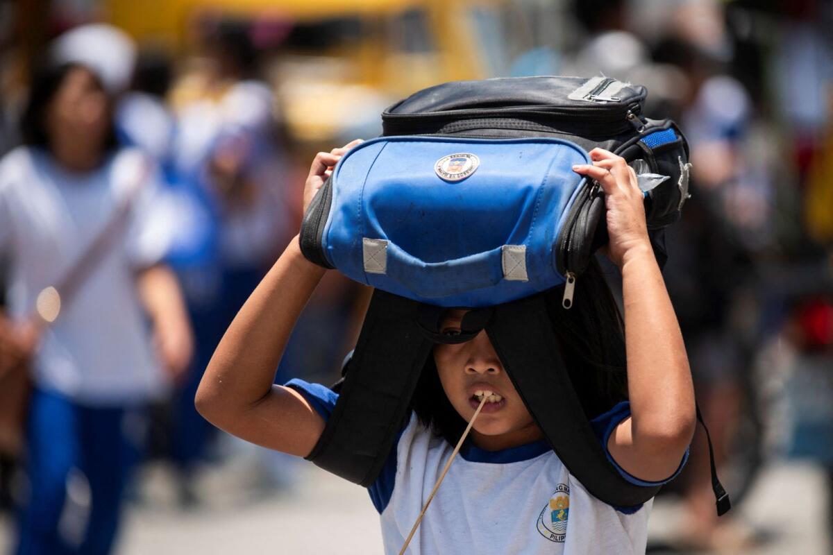 A student uses her bag as protection against the sun, outside an elementary school in Manila, Philippines, on April 19, 2024. — Reuters