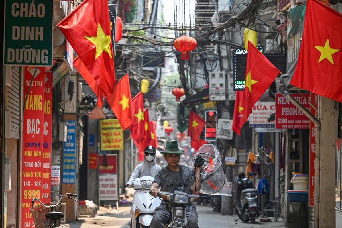 A man carries a fan on a hot day while riding a motorbike along a street lined with Vietnamese national flags in Hanoi on Tuesday. — AFP