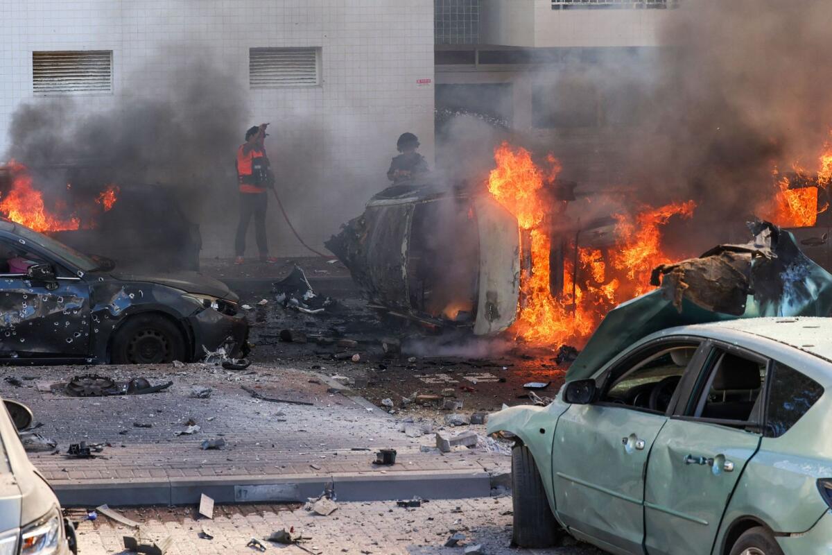 People try to extinguish fire on cars following a rocket attack from the Gaza Strip in Ashkelon, southern Israel, on October 7, 2023. Photo: AFP