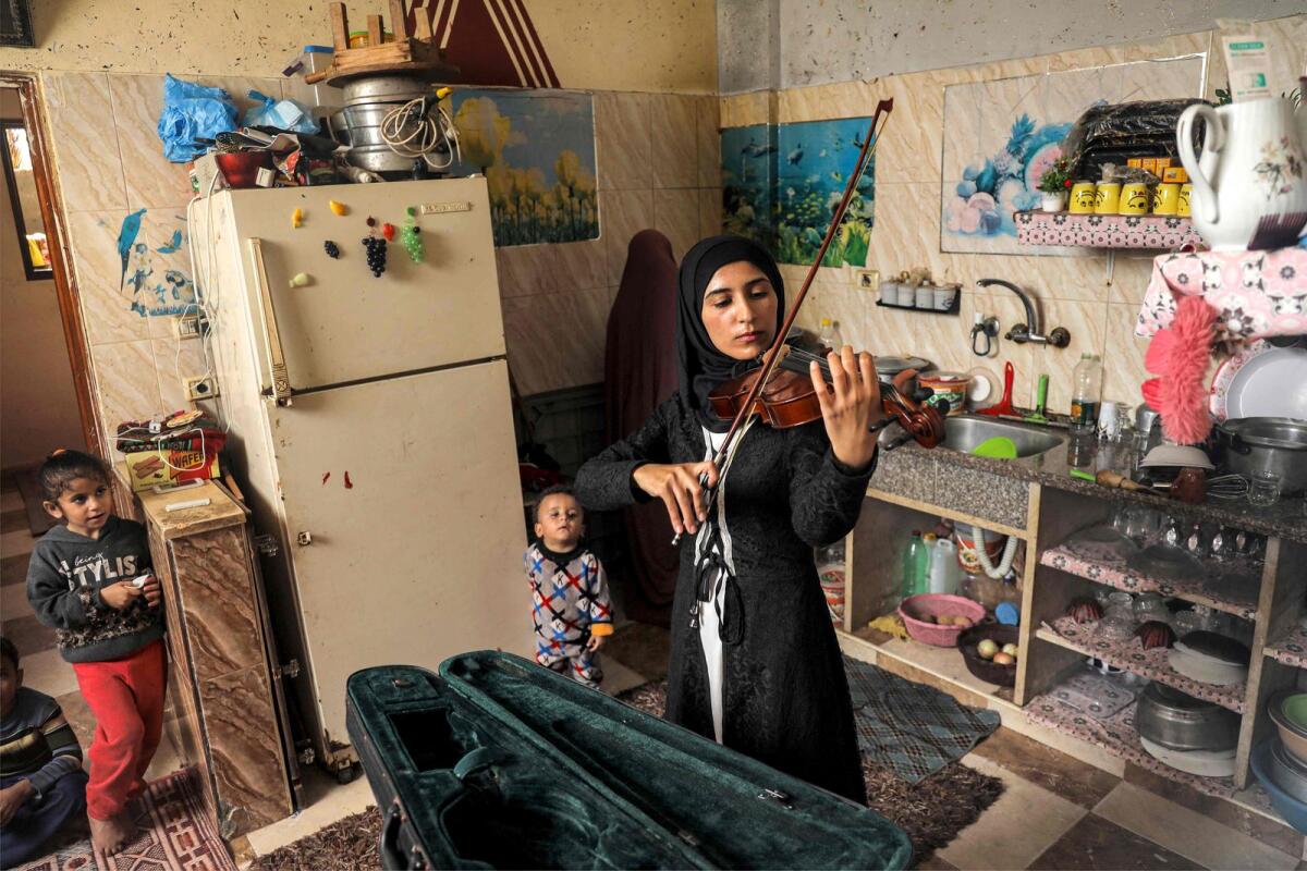 Palestinian musician Jawaher Al Aqraa plays a violin as she stands in the kitchen of her home in Deir Al Balah in the central Gaza Strip on October 24, 2023. — AFP