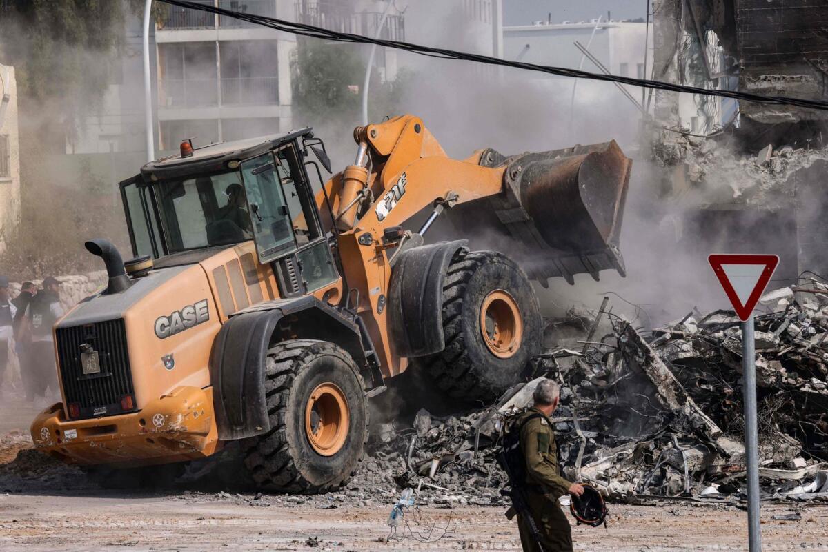 A member of the Israeli security forces looks on as a bulldozer clears rubble in front of a police station in Sderot. Photo: AFP