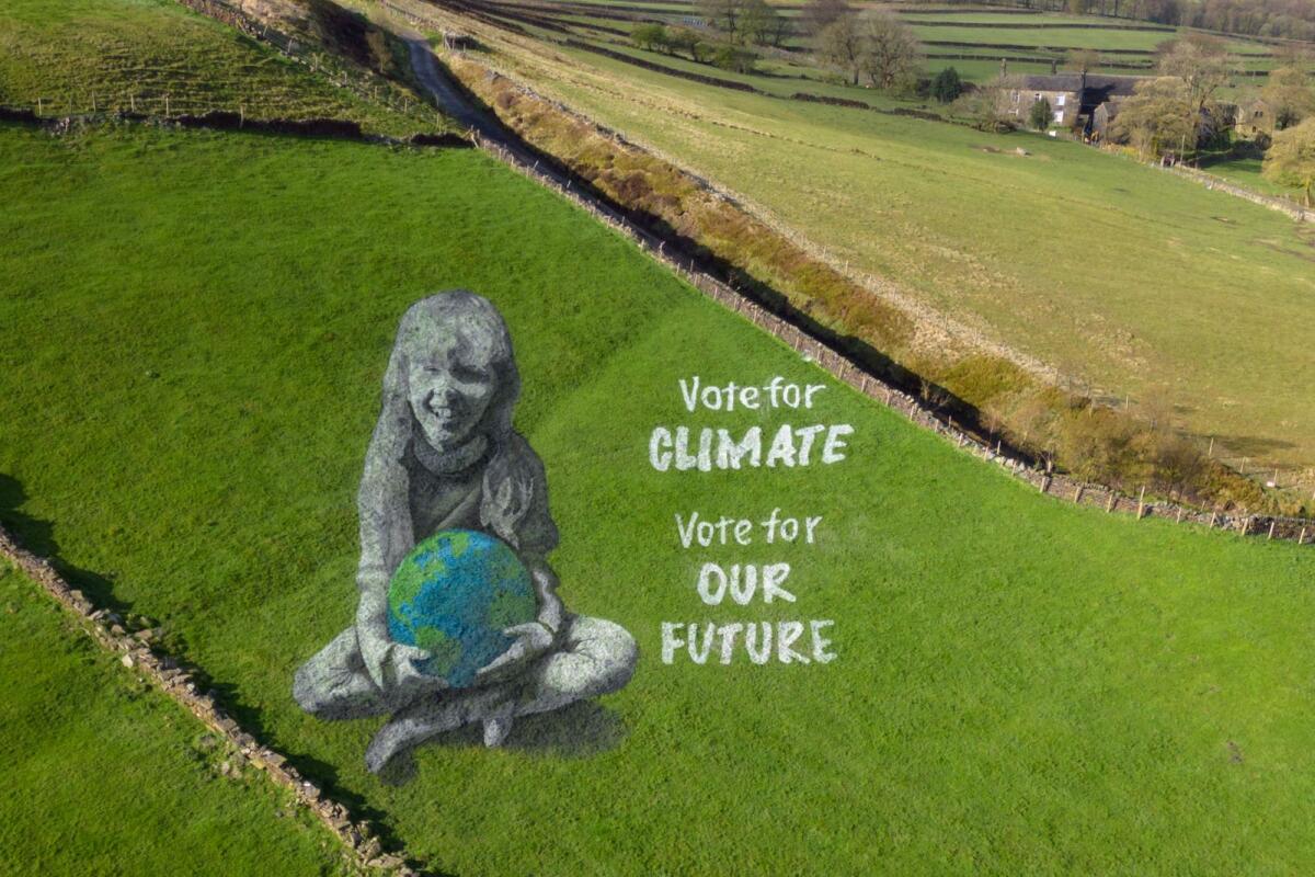 A 50 metre anamorphic field painting of a girl holding the Earth, created by artists from 'Sand In Your Eye' to mark Earth Day, adorns a hillside above Hebden Bridge, north west England on April 19, 2024.  The painting was made over three days using shades of line marker paint used on football pitches. The artwork, bearing the message 'Vote for Climate, Vote for Our Future', was created to coincide with Earth Day 2024 and aims to encourage people to consider the climate when voting in the UK's forthcoming elections. — AFP
