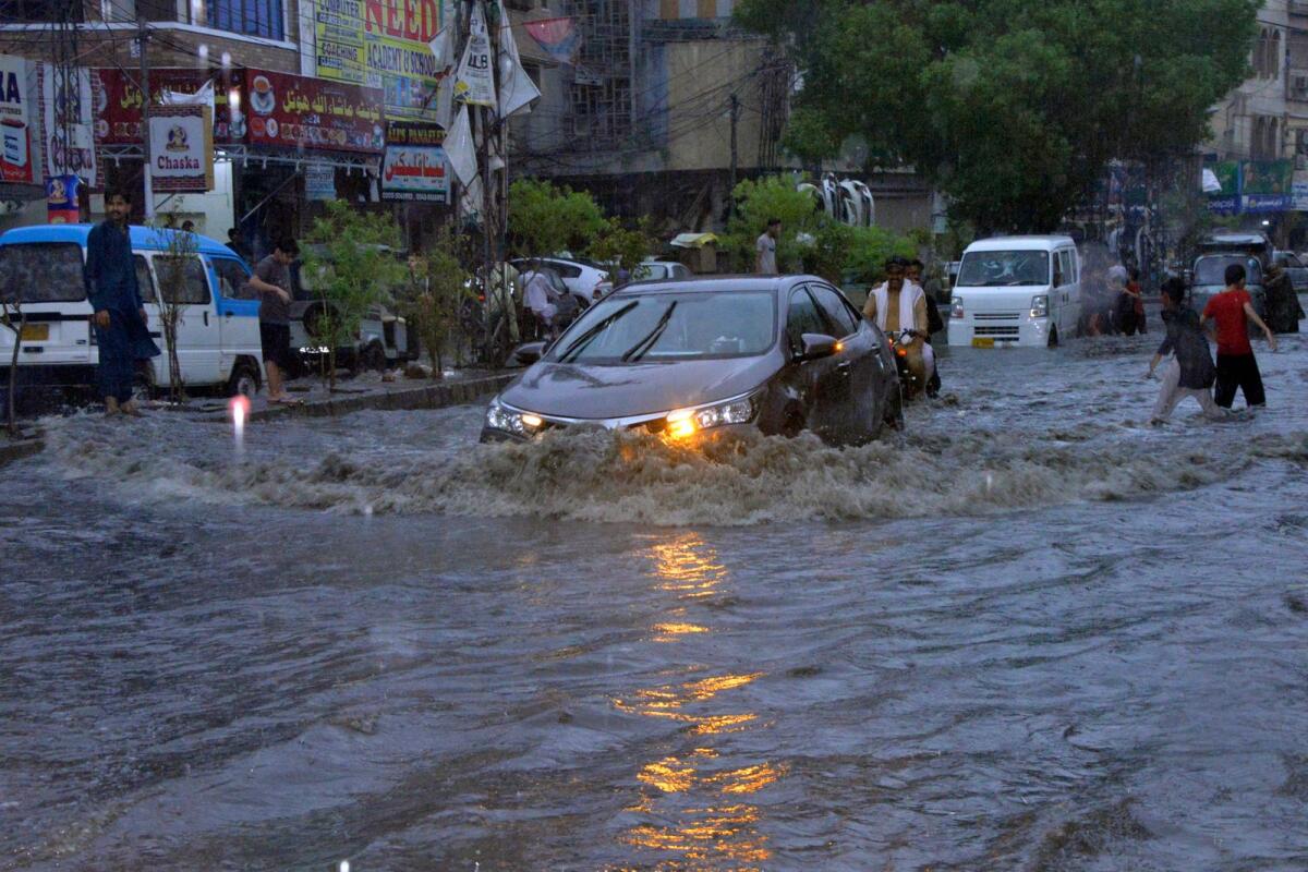 Motorcyclists and cars drive through a flooded road caused by heavy monsoon rainfall in Hyderabad, Pakistan, on Sunday.   --AP