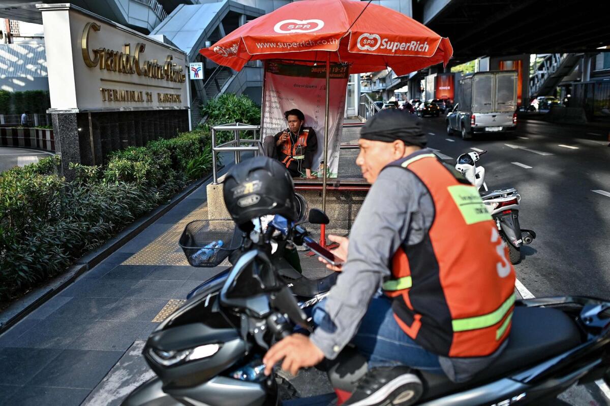 A motorbike taxi driver takes shelter from the sun under an umbrellas as he waits for customers in Bangkok on Monday. — AFP