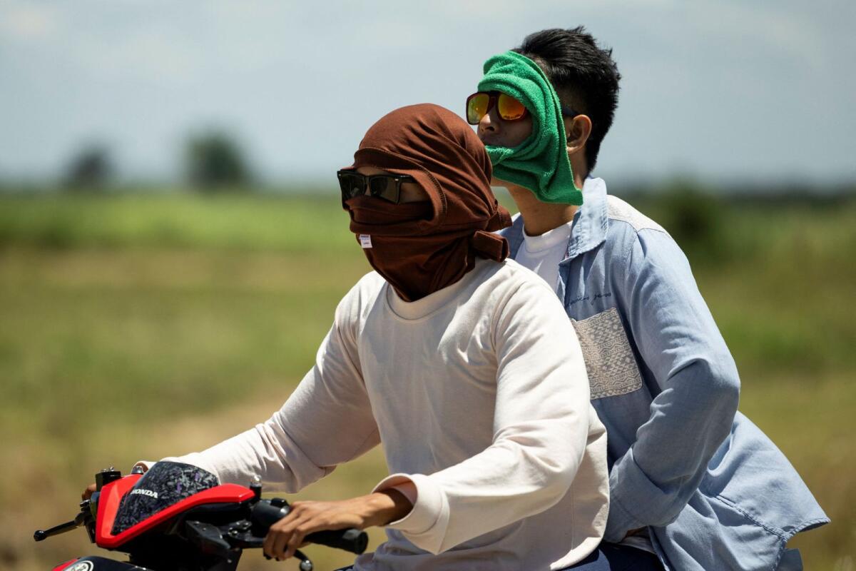 Men wearing clothing to protect against extreme heat ride a motorbike on a road in Candaba, Pampanga, Philippines, on Tuesday. — Reuters