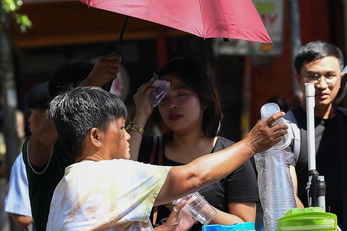 A vendor sells coconut water as a customer (background C) wipes her face during a heatwave in Manila on Monday.  — AFP