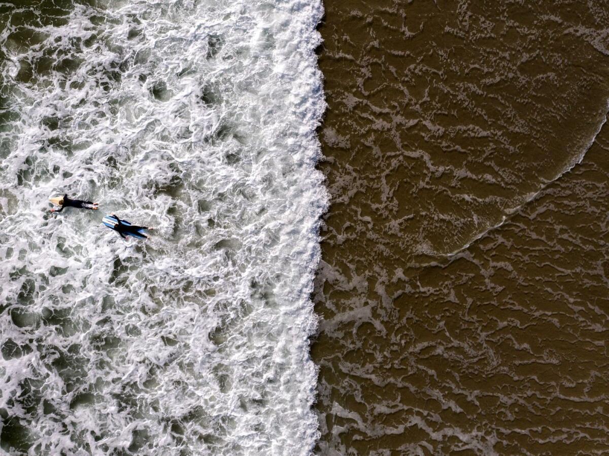 Two surfers wade through water in Huntington Beach, California, on April 17, 2023. — AP